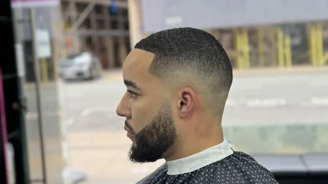 A skin fade with a sharp line-up and a full beard